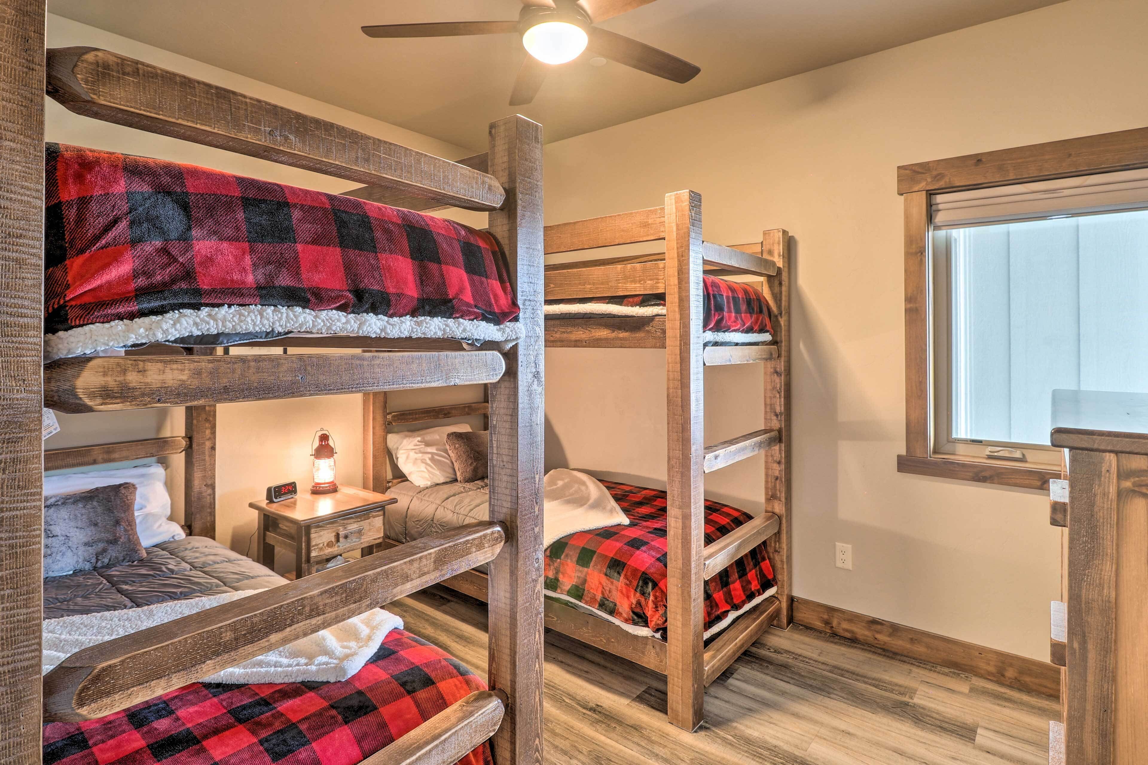 A bunk bed room with a ceiling fan, a bedside table with a lamp, and a window with blinds.