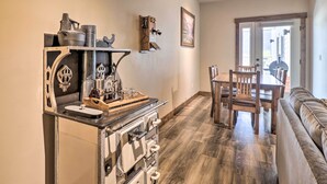 A kitchen with a vintage stove, a coffee machine, and a wooden cabinet. There is a dining area with a table and chairs, and a sofa in the background. - Cozy Columbia Falls Condo w/ Private Balcony! (Columbia Falls)