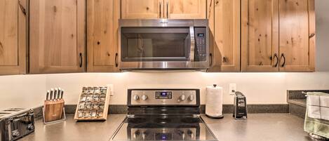 A kitchen with wooden cabinets, a stainless steel microwave, a stove, a toaster, and a knife block.