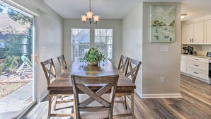 Une salle à manger avec une table et des chaises en bois, un lustre et une vue sur le jardin à travers de grandes fenêtres.