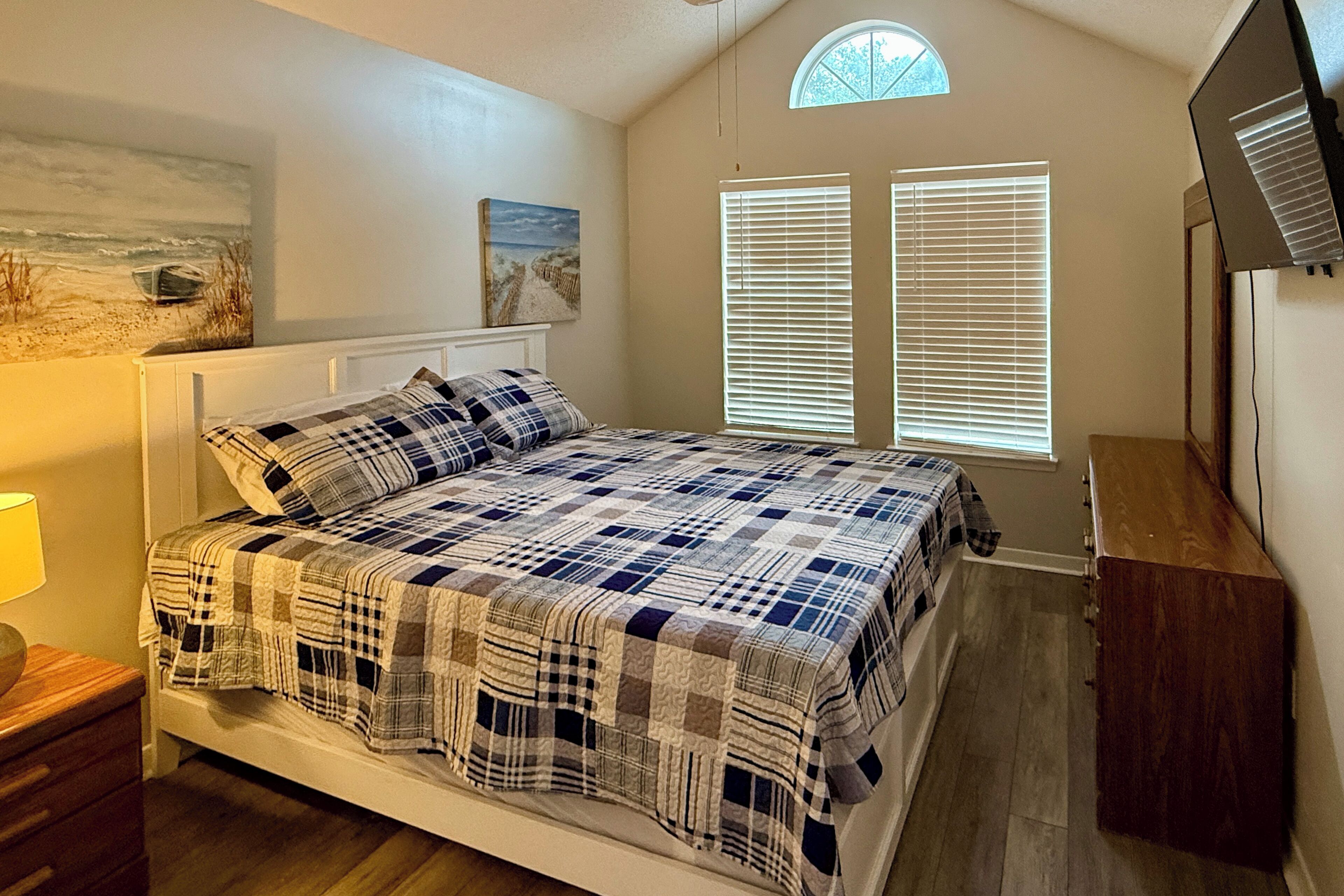 A bedroom with a bed, a nightstand, a dresser, a painting, and a window with blinds.