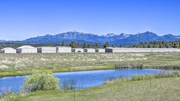 A rural setting with a row of buildings, a small pond, and mountains in the background.