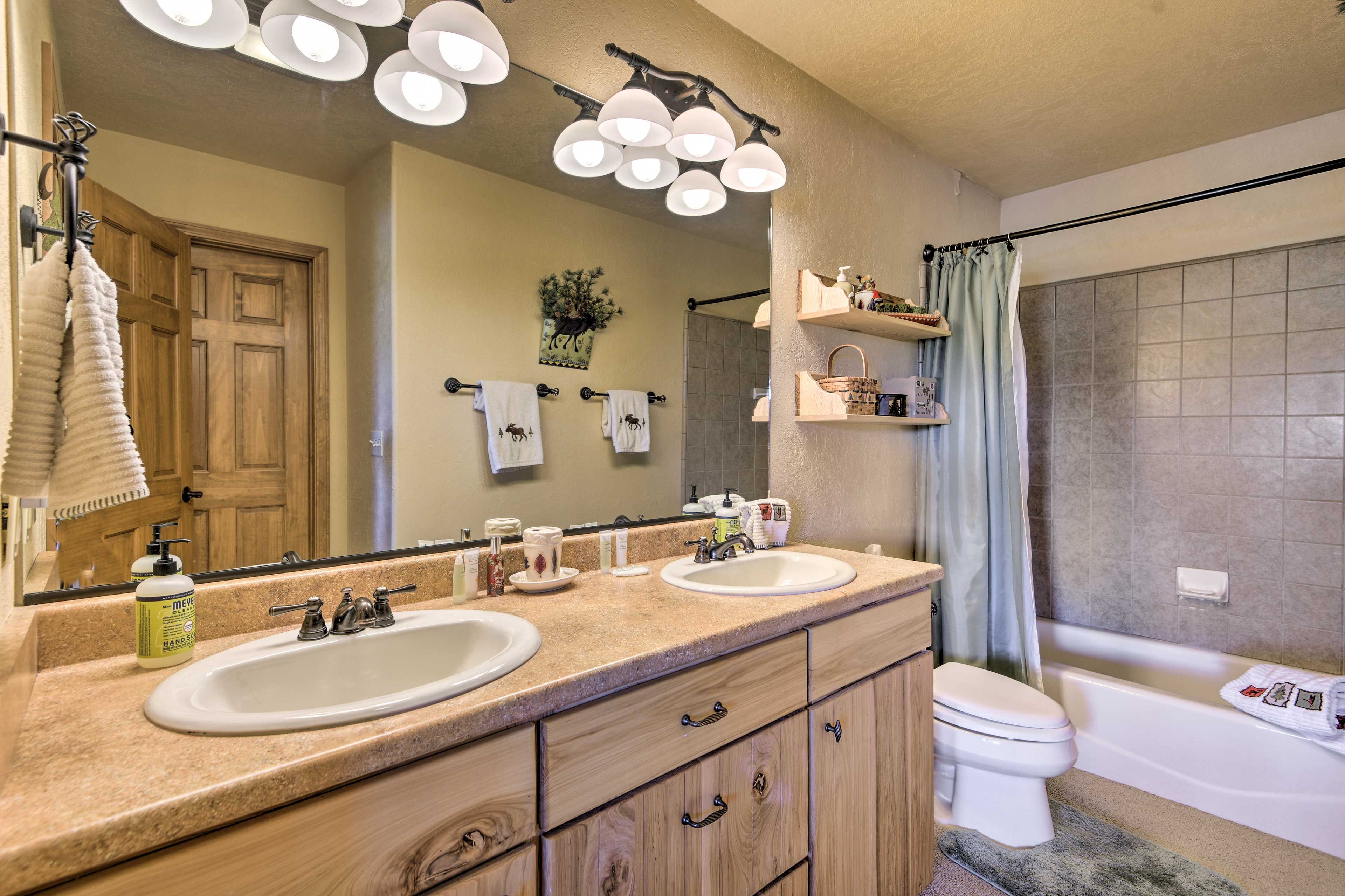 Une salle de bain avec deux lavabos, des toilettes et une baignoire. On y trouve des luminaires au plafond, un porte-serviettes et un miroir.