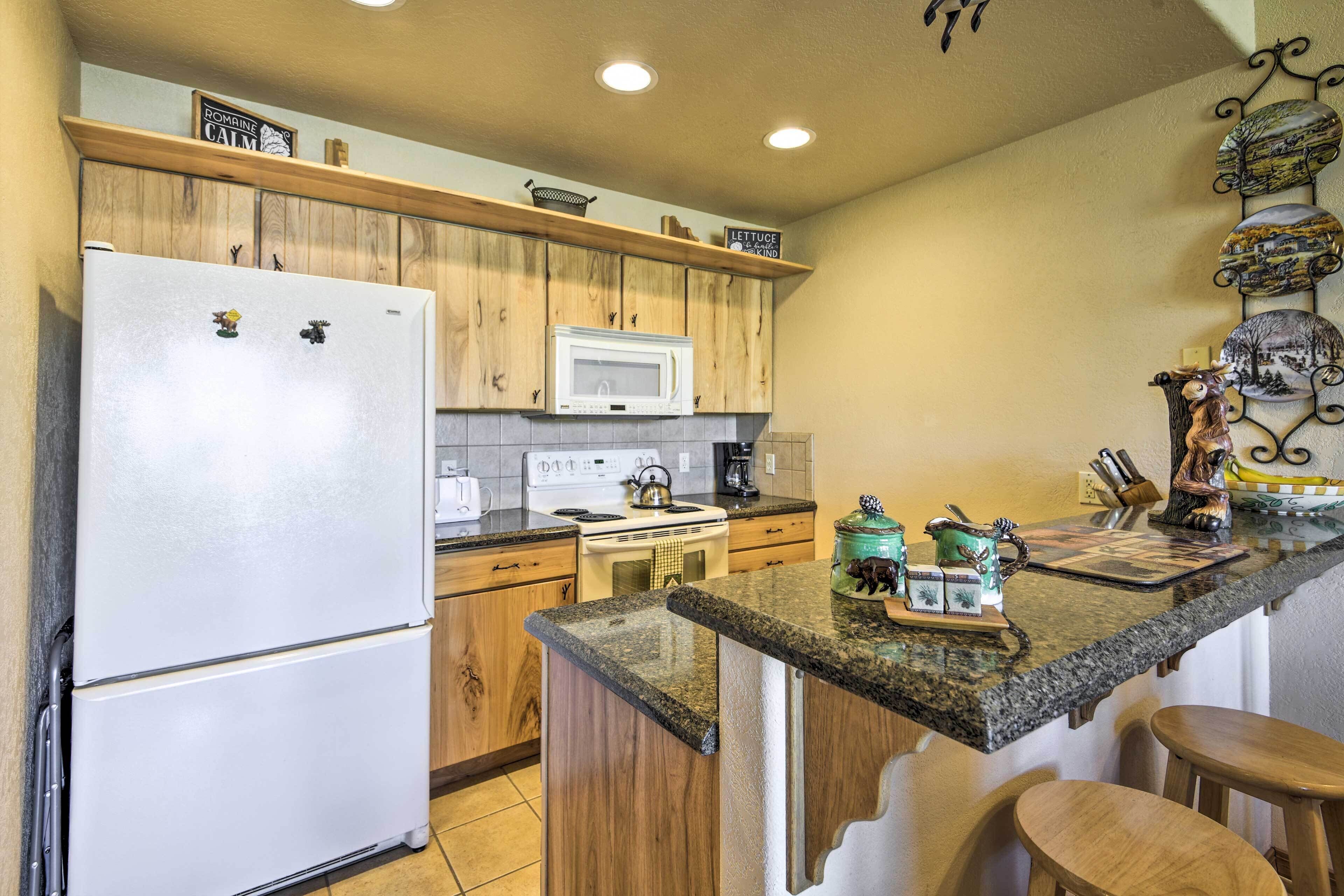 A kitchen with wooden cabinets, a white refrigerator, a microwave, a stove, and a granite countertop.