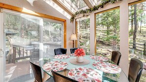 A glass-top dining table with floral placemats, surrounded by chairs, in a room with large windows overlooking a forested area. - 330760: Home w/ Hot Tub - 11 Mi to Rainbow Falls (Woodland Park)