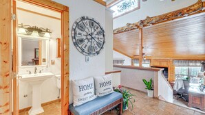 A bathroom with a sink, mirror, and a large wall clock. There is a bench with pillows that say "HOME SWEET HOME" and a potted plant. - 330760: Home w/ Hot Tub - 11 Mi to Rainbow Falls (Woodland Park)