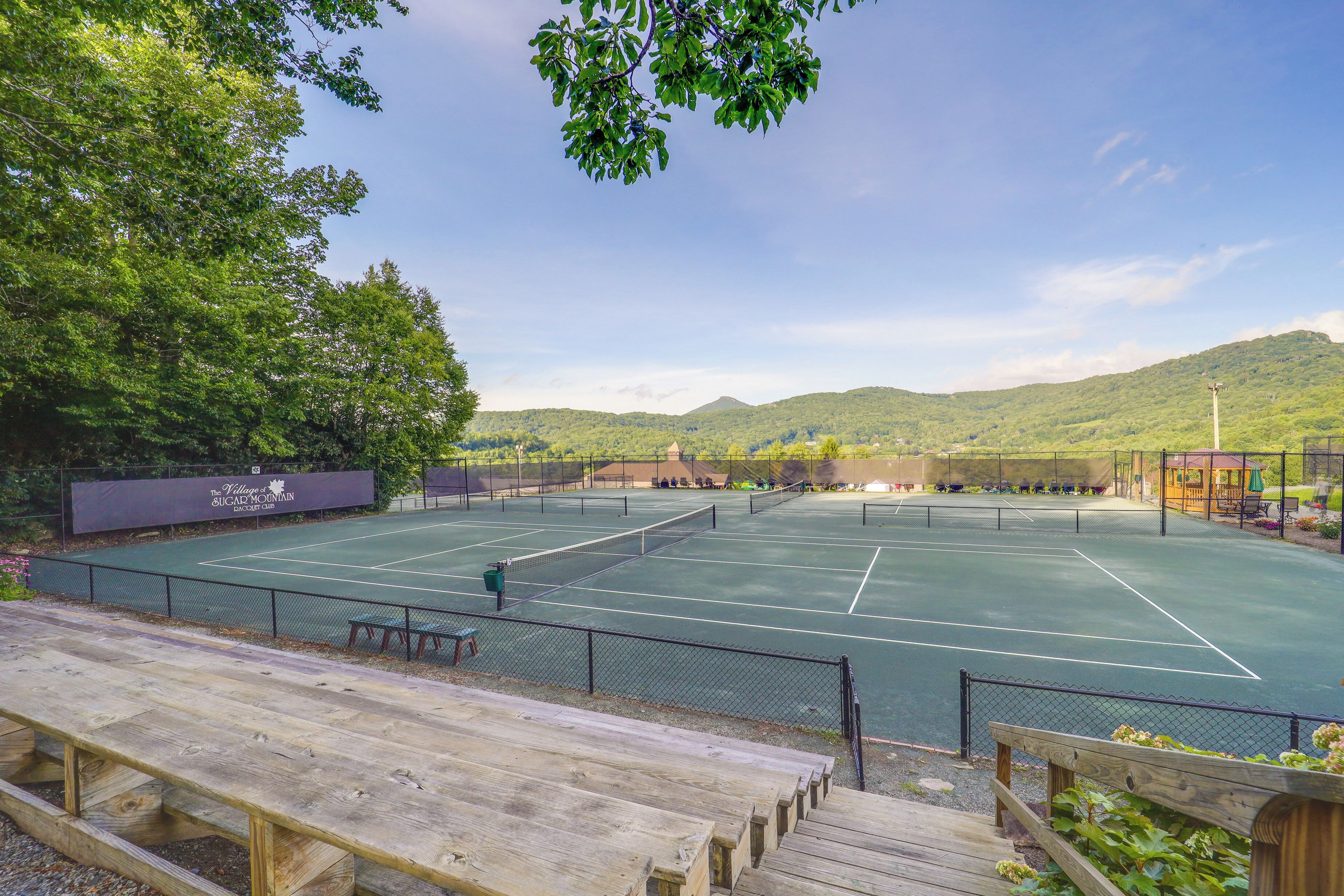 A tennis court with a wooden bench area and a fence.