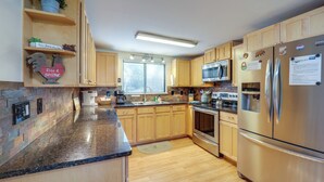 A kitchen with wooden cabinets, granite countertops, stainless steel appliances, and a window with blinds. - Walk to Ski & Golf: Sugar Mountain Condo! (Banner Elk)