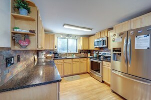 Una cocina con armarios de madera, encimeras de granito, electrodomésticos de acero inoxidable y una ventana con persianas.