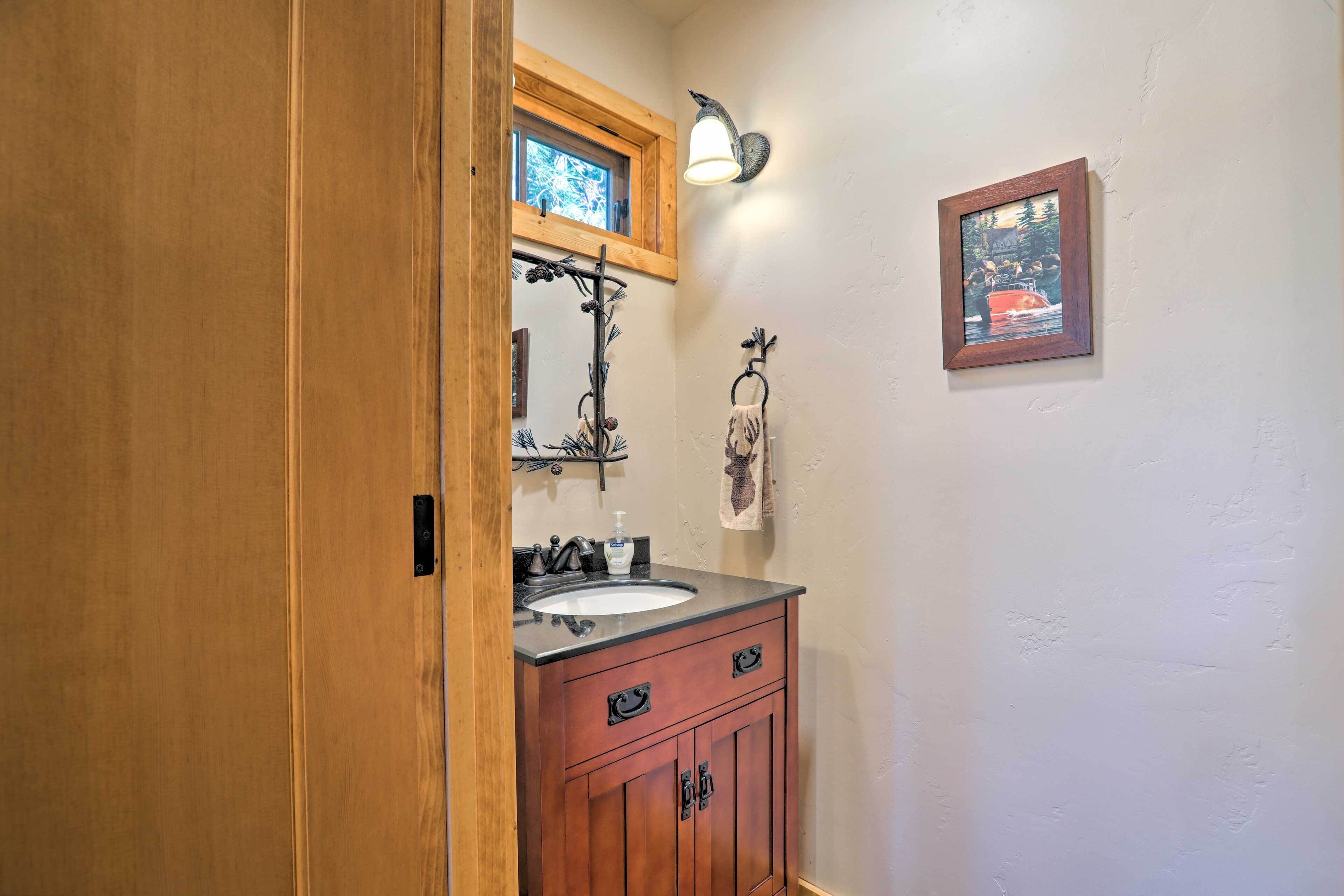 Una puerta de madera que da a un baño con lavamanos, tocador y perchero para toallas.