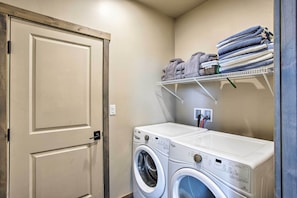 A laundry room with a front-loading washer and dryer, a door, and a shelf with folded towels. - Upscale Moab Townhome w/ Hot Tub: 20 Min to Arches (Moab)
