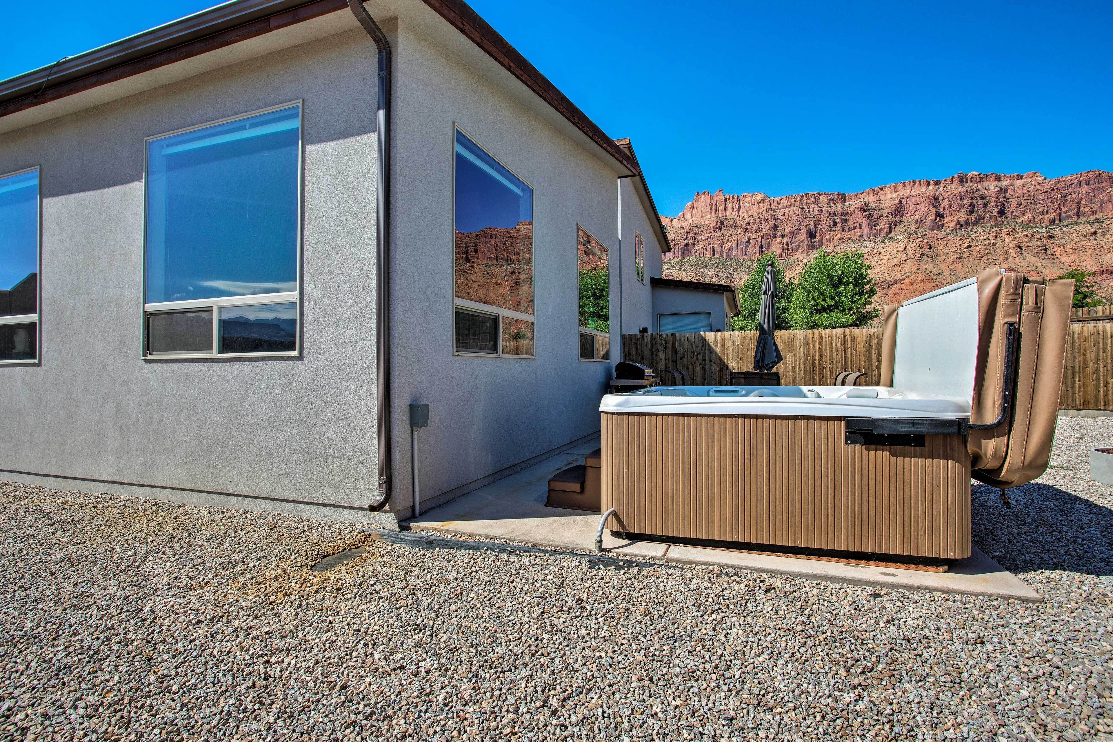 A modern building with large windows, a hot tub, and a view of red rock formations.