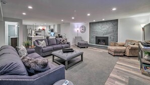A modern living room with a grey sofa, ottoman, and armchair, a fireplace, and a kitchen in the background. - Near Snowbird & Alta Resorts: Winter Getaway (Salt Lake City)