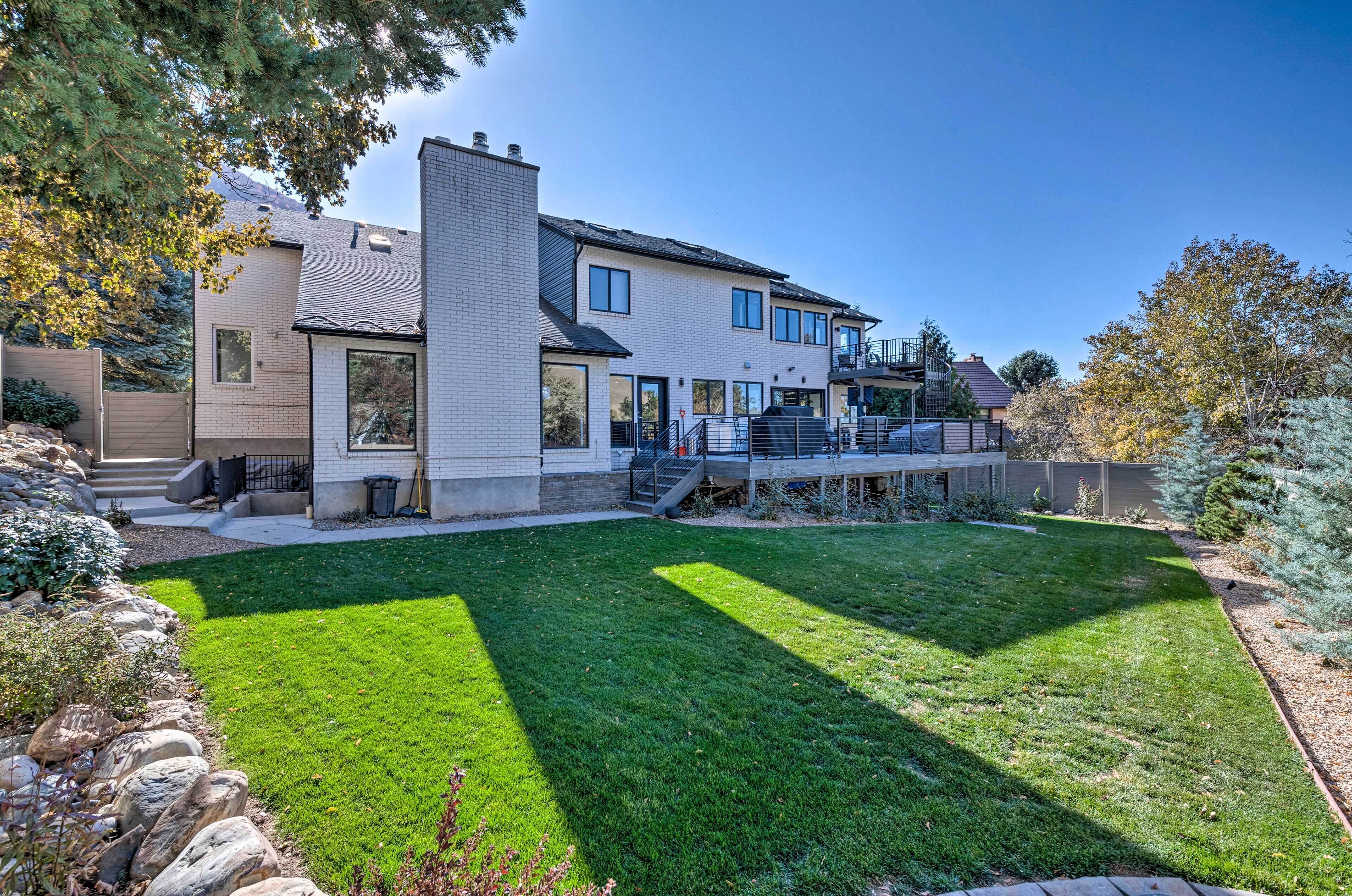 A modern two-story house with a well-maintained lawn, a stone retaining wall, and a staircase leading to a deck.