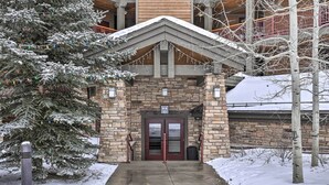 A building entrance with a stone facade, a wooden upper level, and a snow-covered tree.