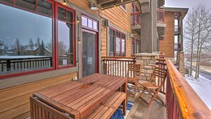 A wooden deck with a table and chairs, large windows, and a stone wall.