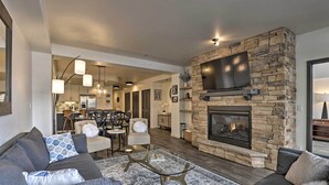 A modern living room with a stone fireplace, a large flat-screen TV, and a cozy seating area with a sofa and armchairs.