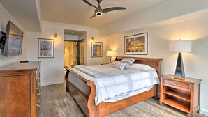 A bedroom with a wooden bed, a nightstand with a lamp, a ceiling fan, and framed pictures on the walls.