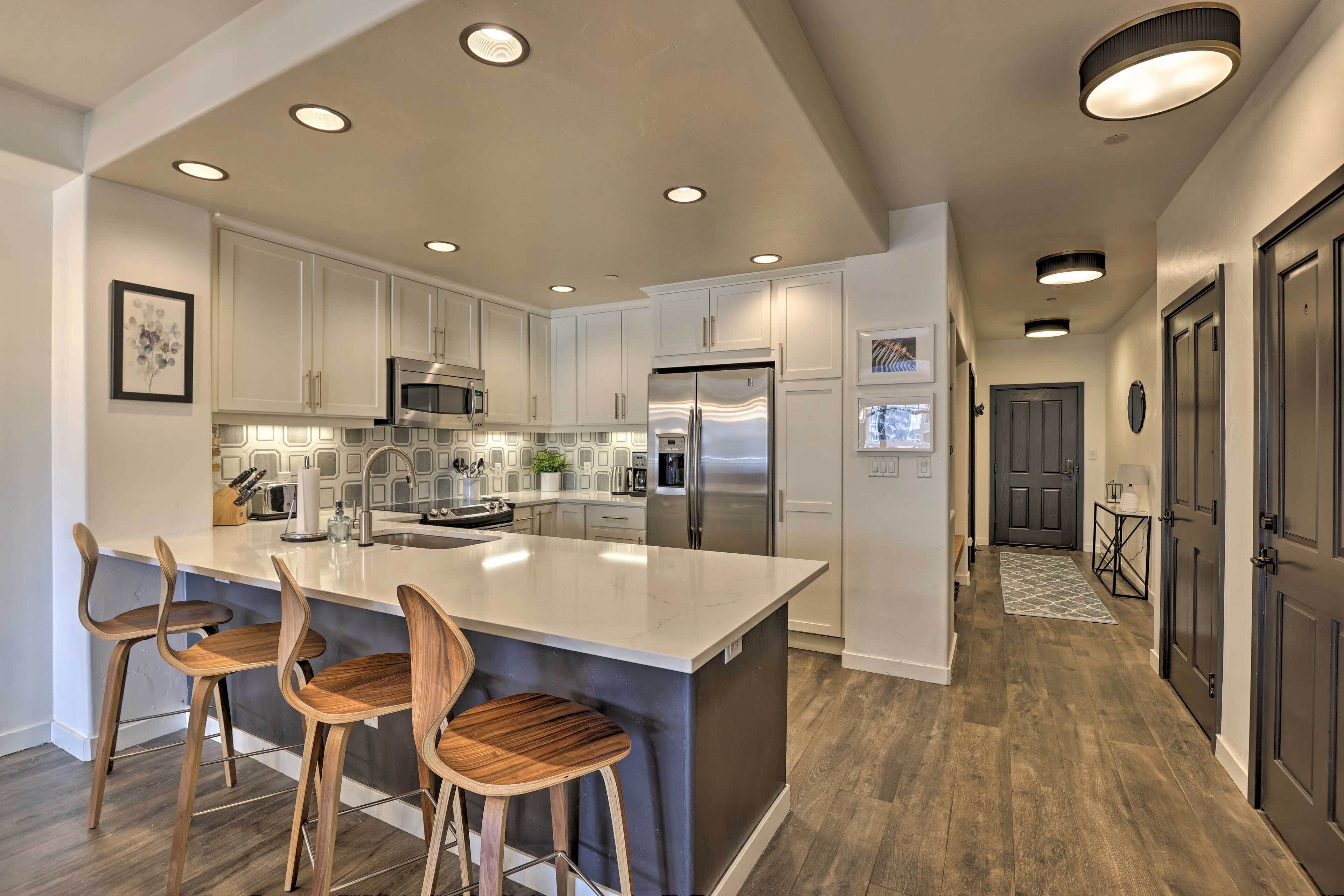 A modern kitchen with a large island, stainless steel appliances, and wooden bar stools.