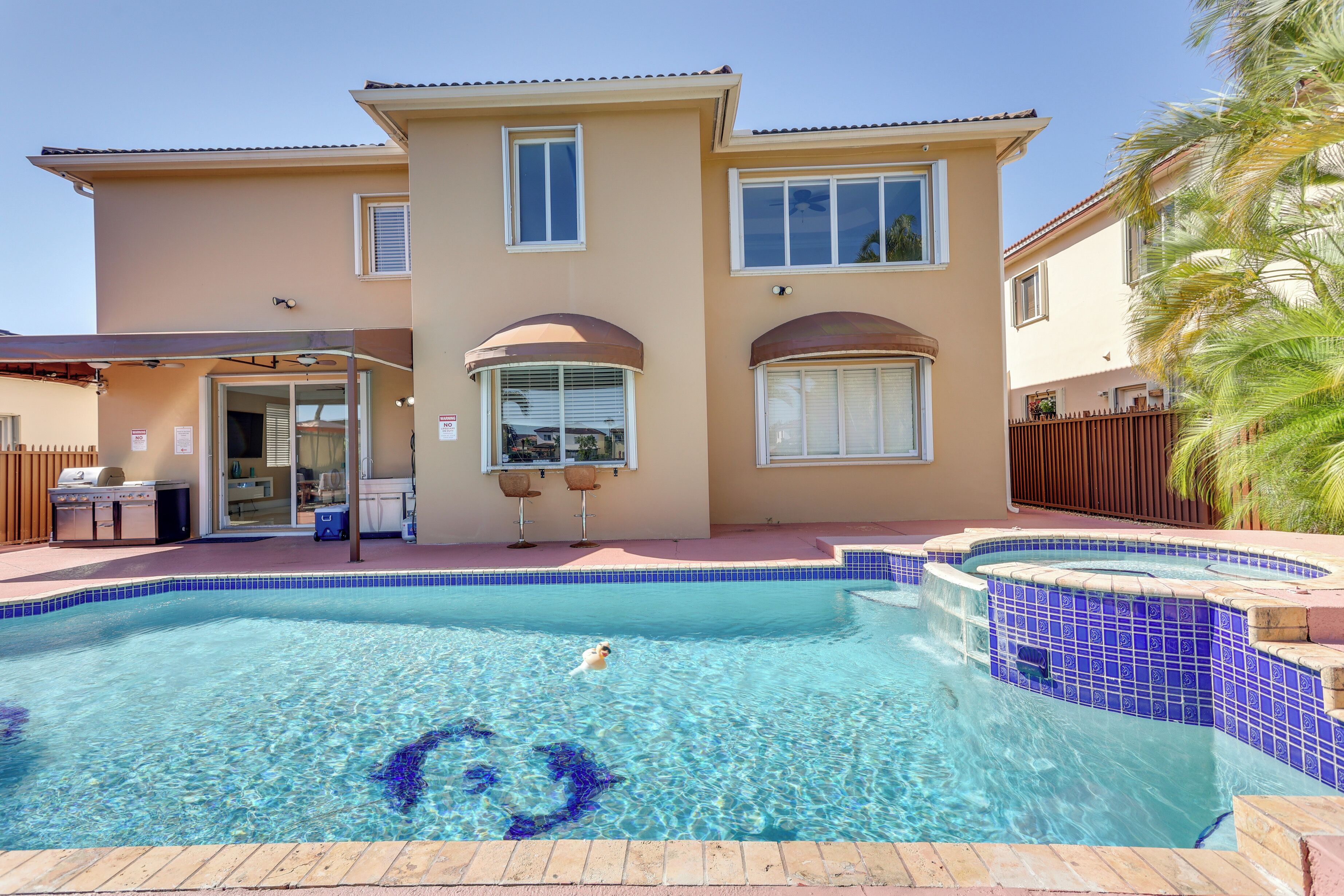 A two-story house with a swimming pool, a patio with outdoor furniture, and a fenced backyard.