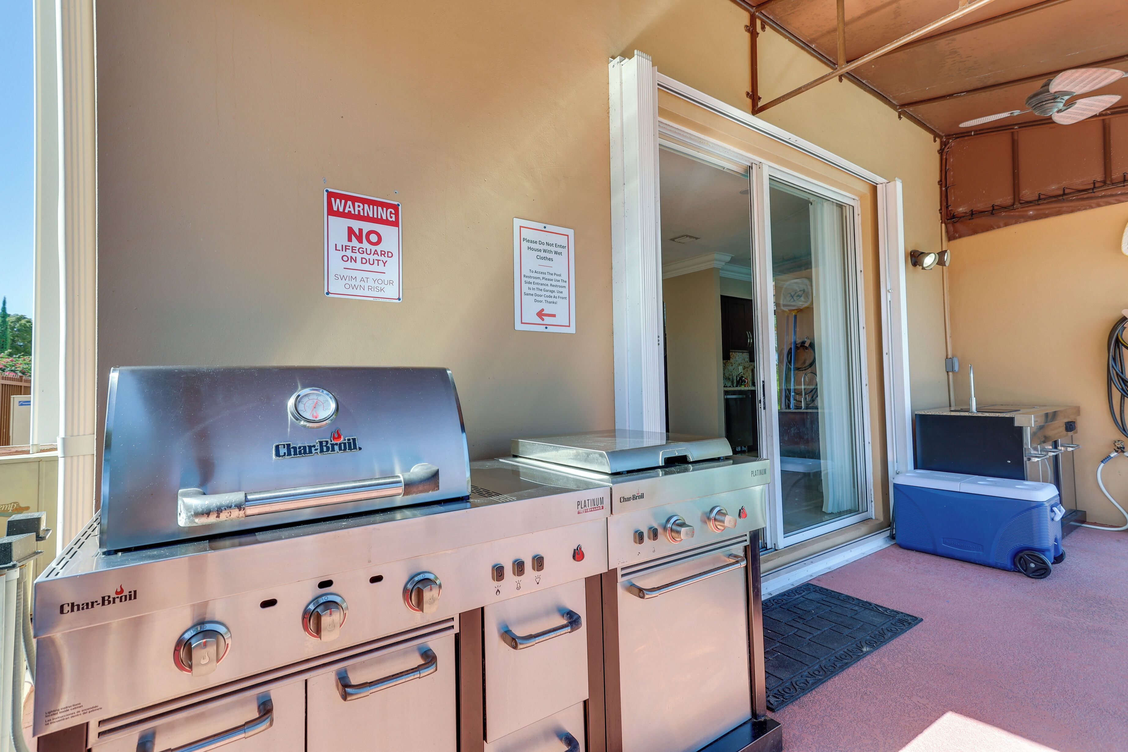 A Char-Broil grill and oven set up in a covered outdoor area with a sliding glass door and a blue cooler.