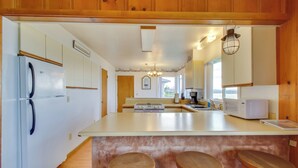A kitchen with wooden cabinets, a white refrigerator, a microwave, and a large island with stools. - Rustic Coastal Smith River Cottage w/ Ocean Views! (Smith River)