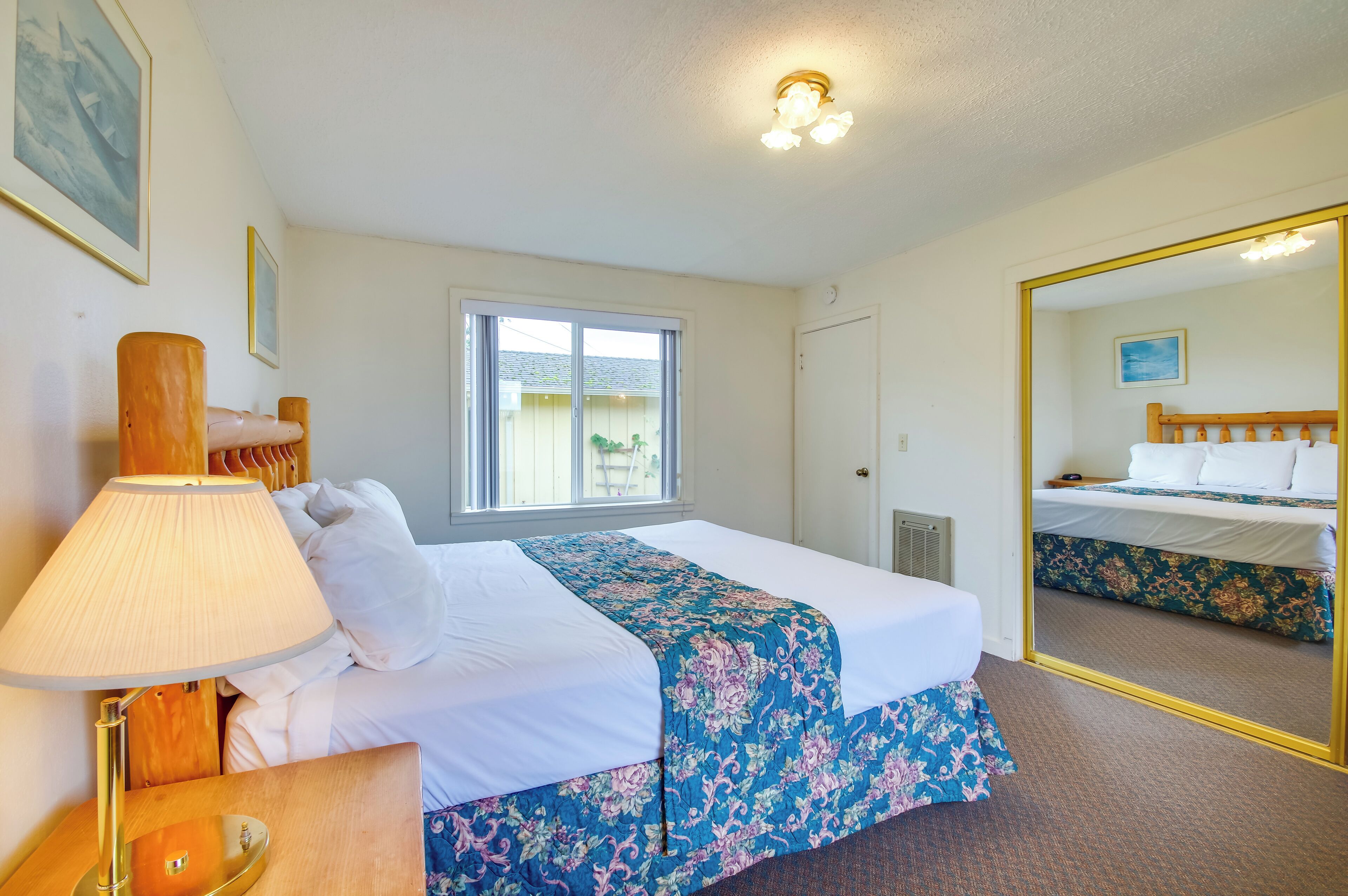 Una habitación de hotel con cama, lámpara de noche, ventana y espejo.