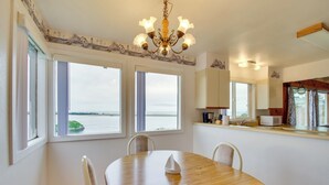 A dining area with a wooden table, chairs, a chandelier, and large windows overlooking a body of water. - Rustic Coastal Smith River Cottage w/ Ocean Views! (Smith River)