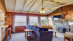 A cozy cabin interior with a sofa, wooden tables, a fireplace, and a stone wall. - Rustic Coastal Smith River Cottage w/ Ocean Views! (Smith River)