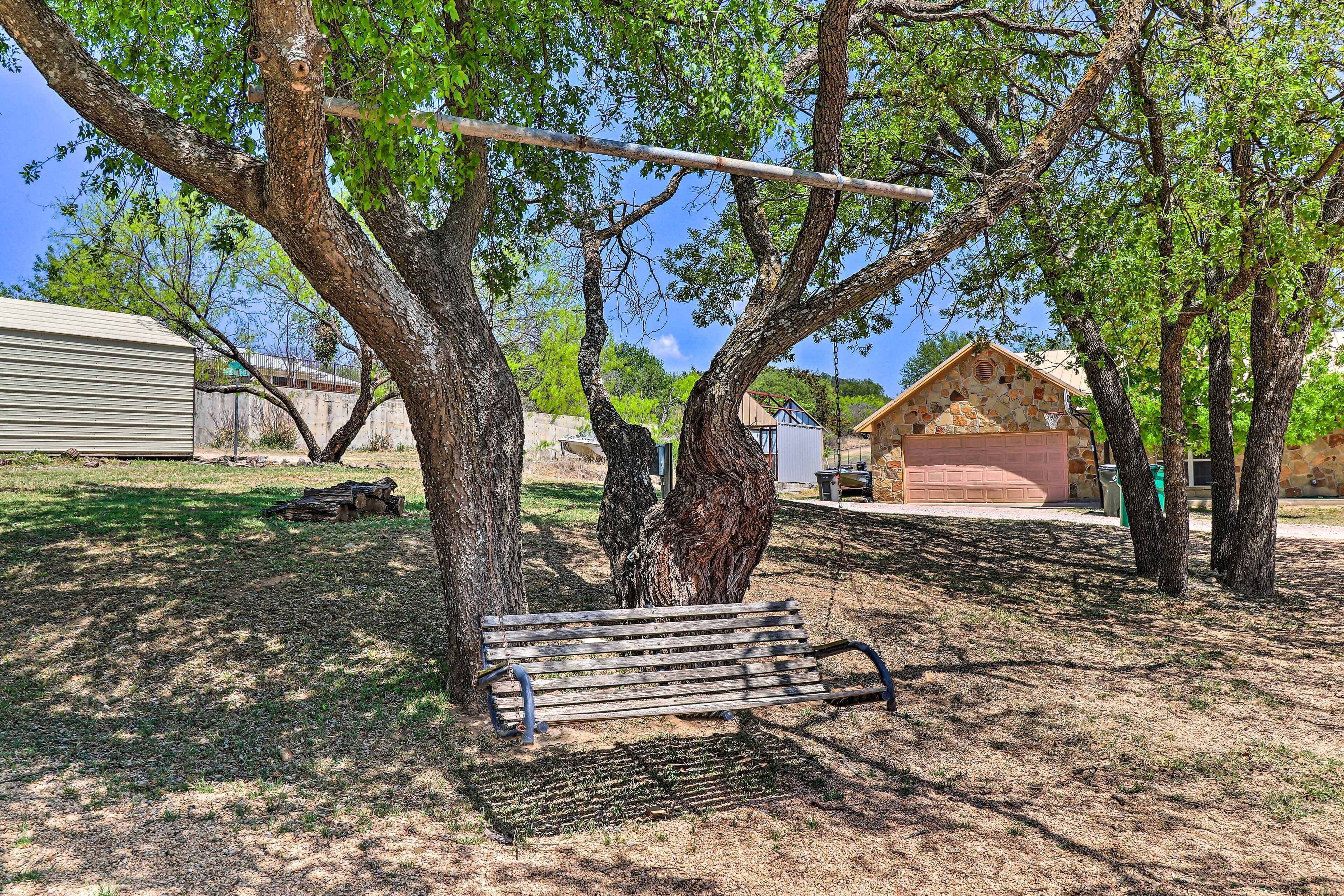A park bench under a tree, surrounded by grass and a stone building.