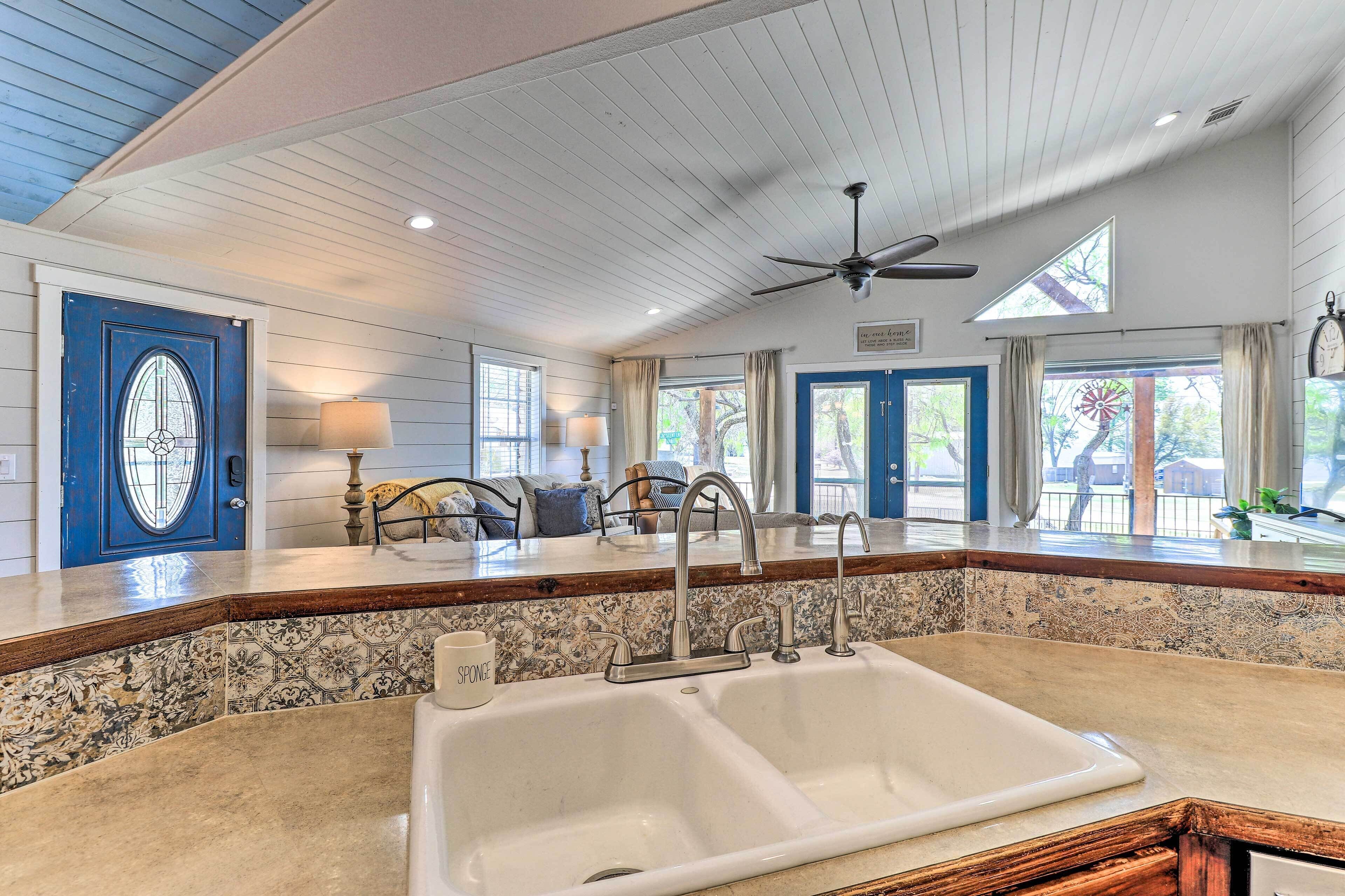 A kitchen with a double sink, a ceiling fan, and a view of the outdoors through large windows.