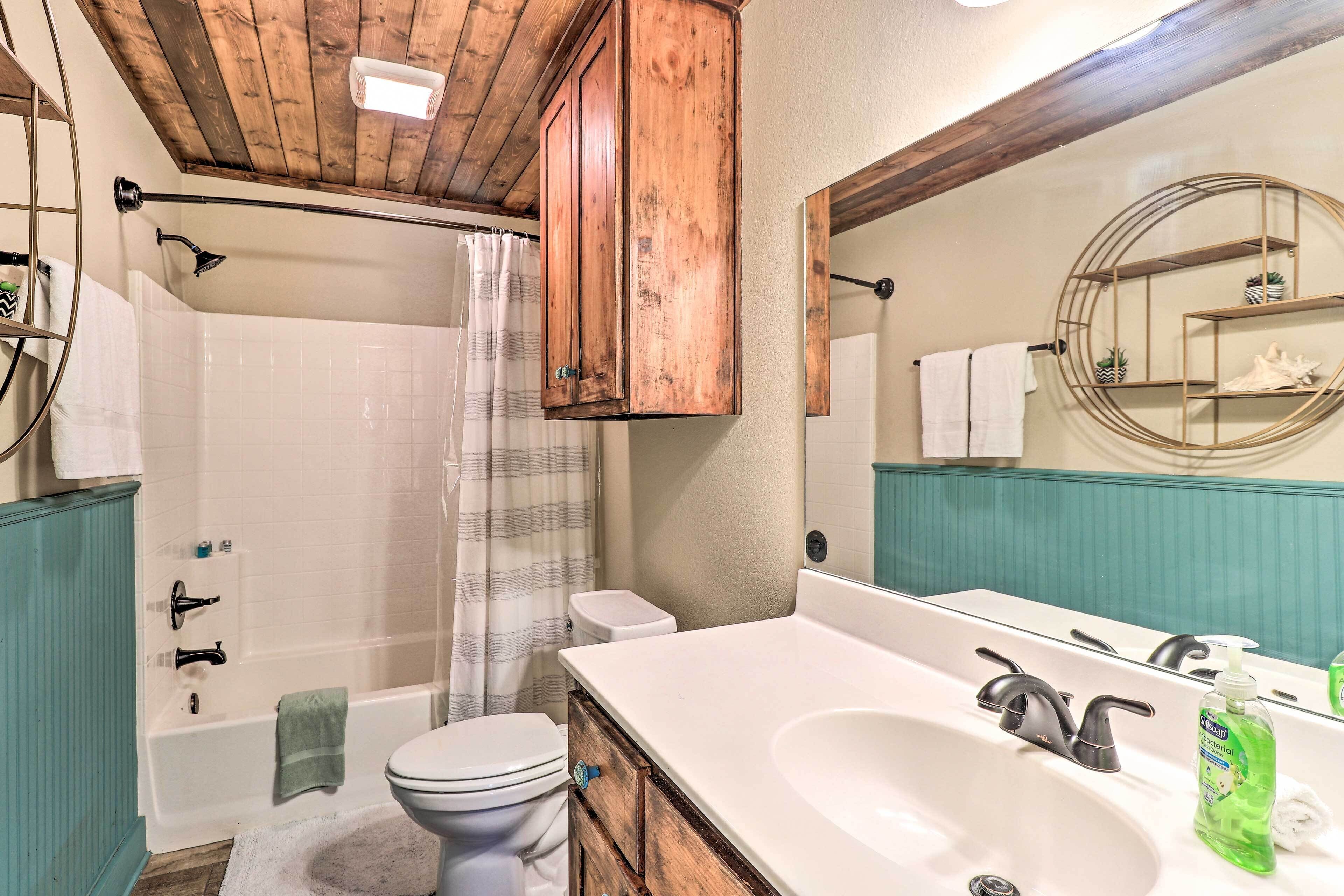 Un bagno con soffitto in legno, una vasca da bagno bianca, un water e un lavandino con uno specchio sopra.