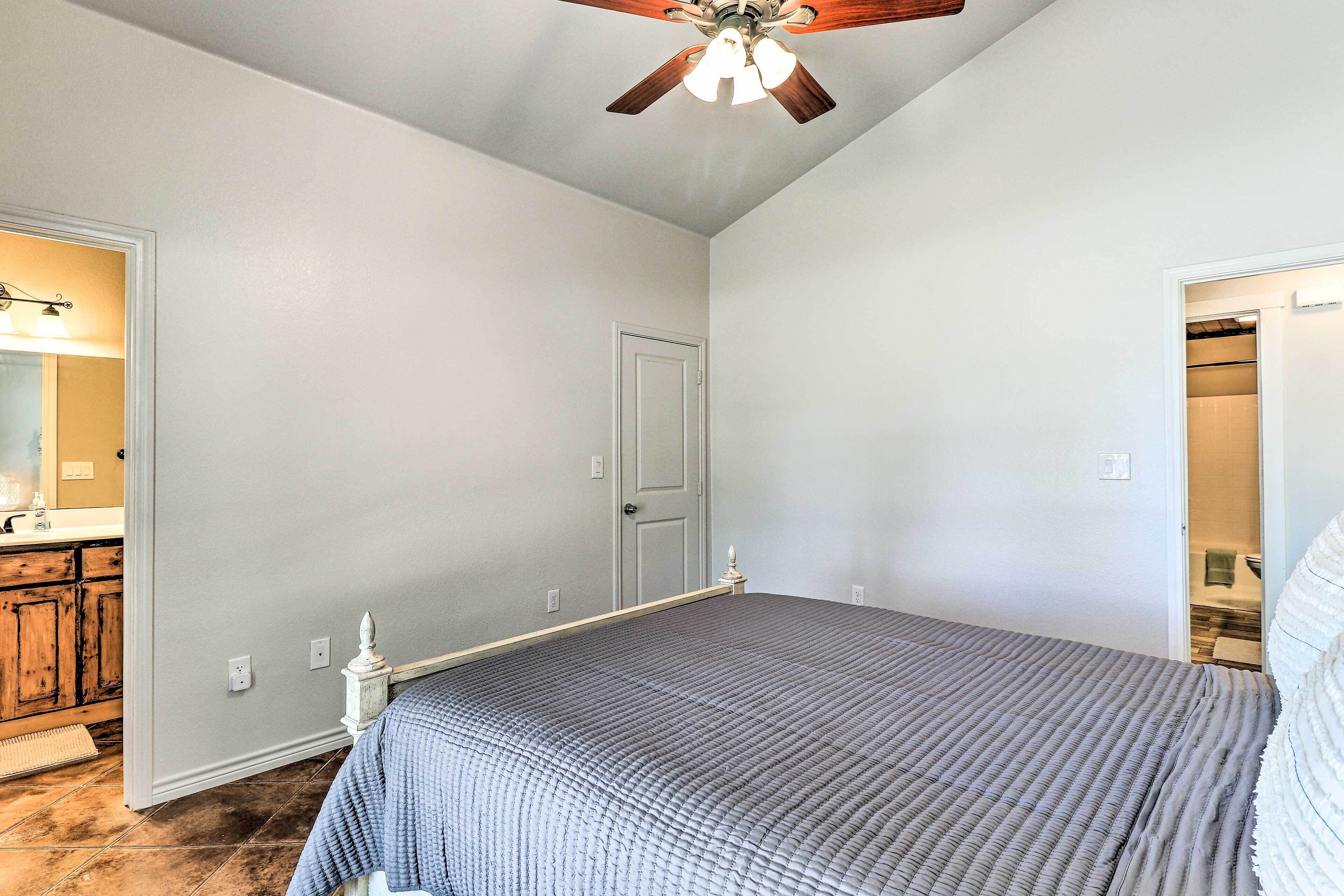 A bedroom with a bed, a ceiling fan, and a door leading to a bathroom.