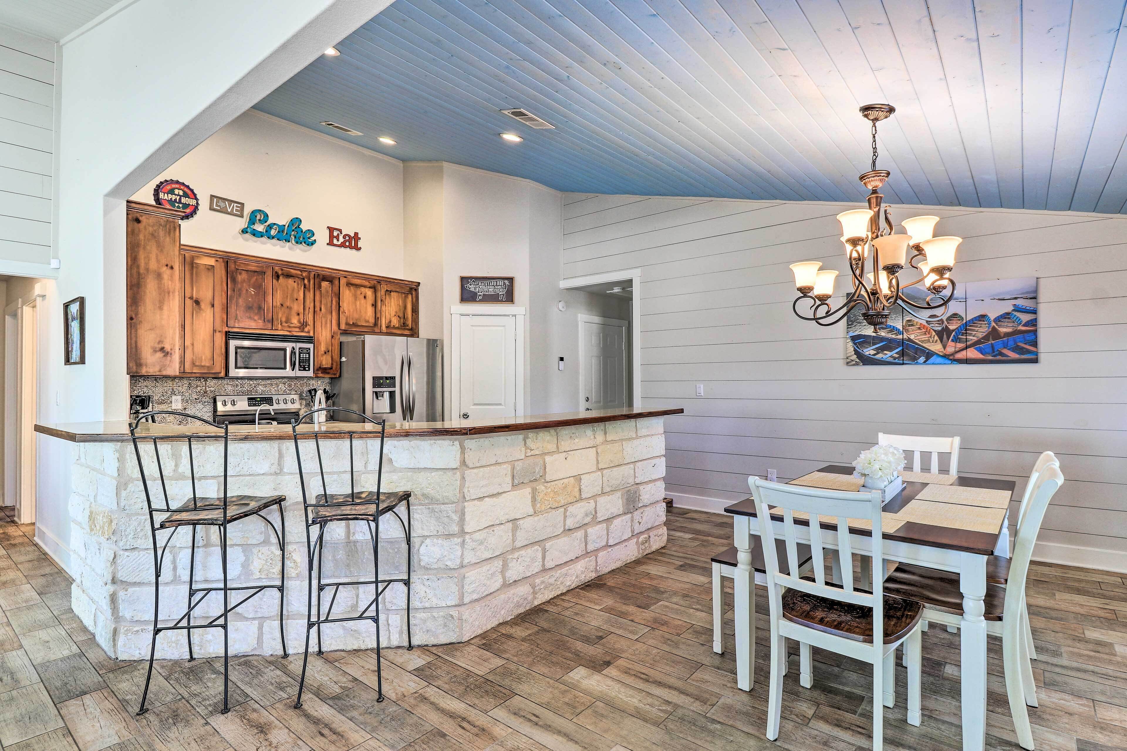 A kitchen with a stone island, wooden cabinets, and a dining area with white chairs and a table.