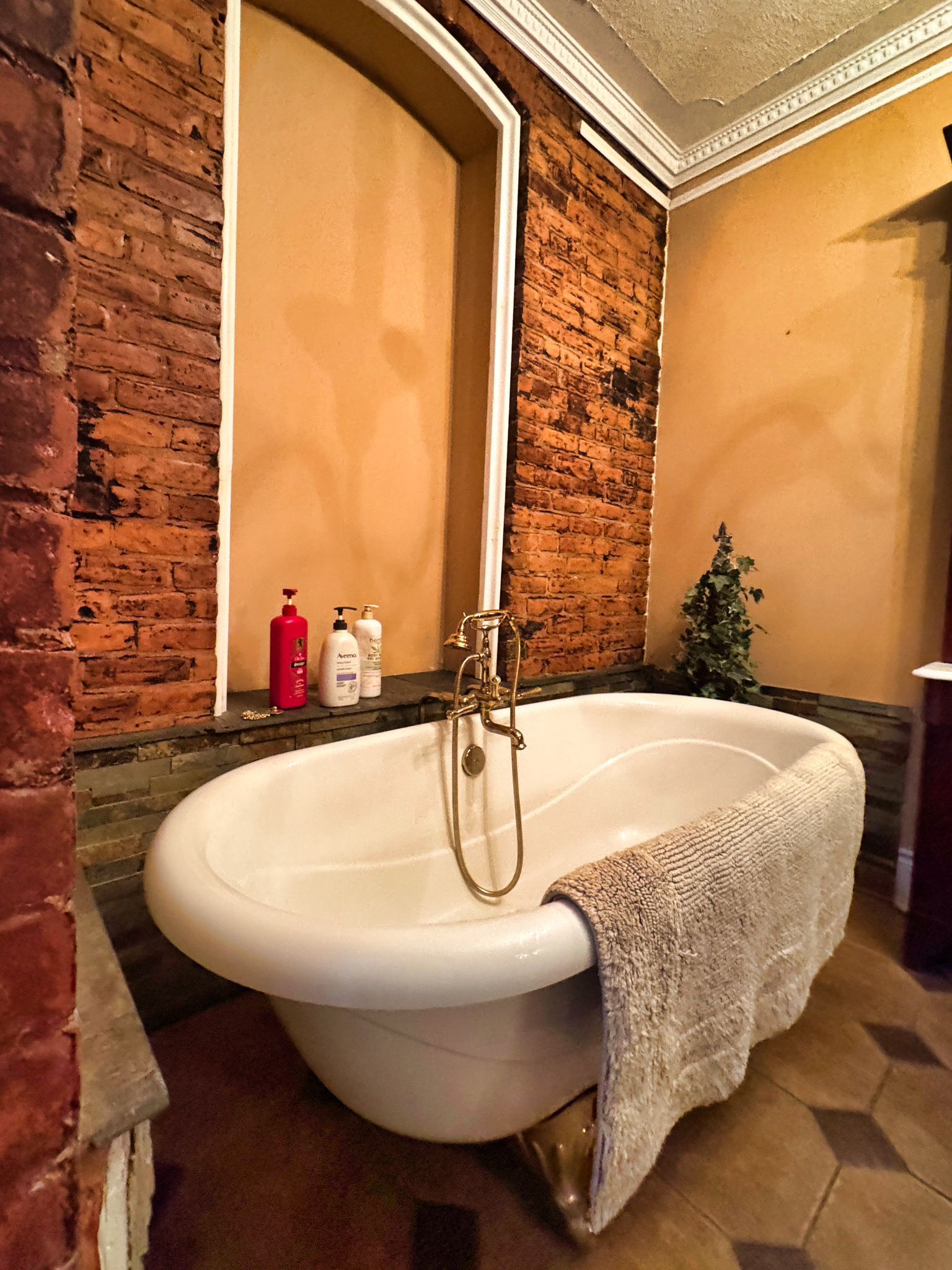 A bathroom with a freestanding bathtub, a brick wall, and a mirror.