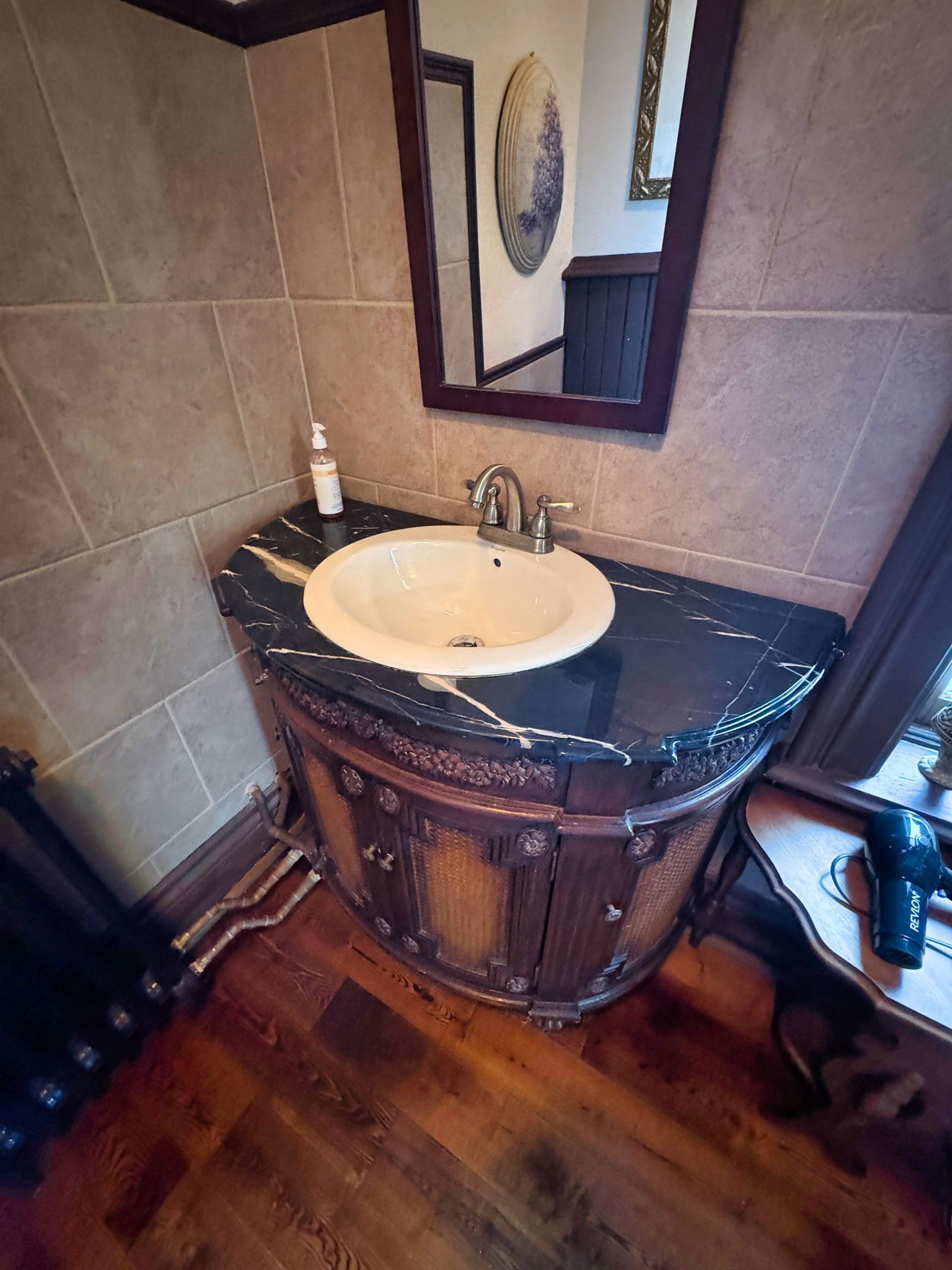 Un baño con lavamanos de mármol, tocador de madera y espejo sobre el lavamanos.