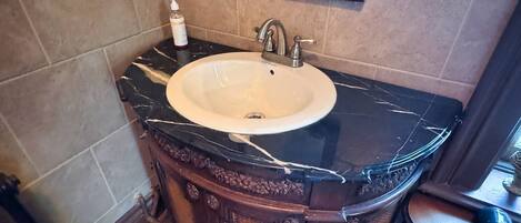 Un baño con lavamanos de mármol, tocador de madera y espejo sobre el lavamanos.