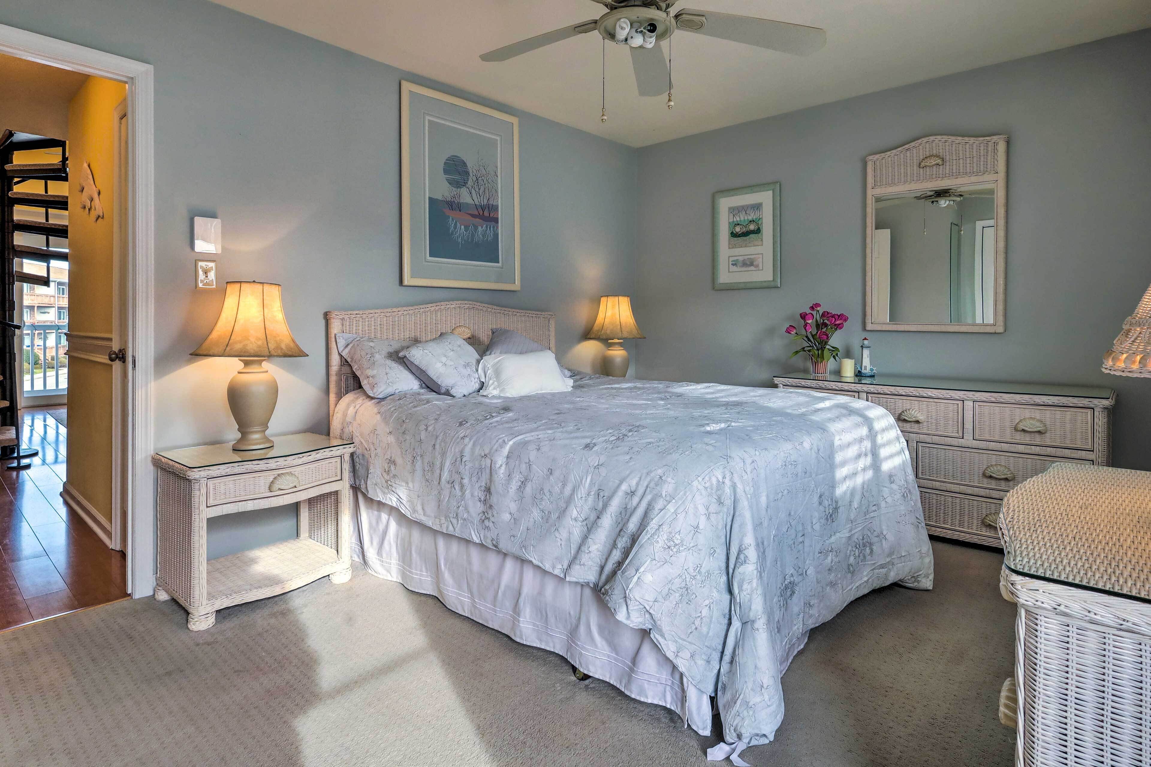 Une chambre à coucher comprenant un lit, des tables de chevet, une commode, un miroir et un ventilateur de plafond.