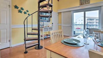 A dining area with a wooden table set for two, a spiral staircase, and a view of the outside balcony.