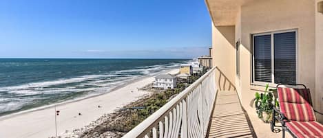 A balcony with a view of the beach, a chair, and a potted plant.