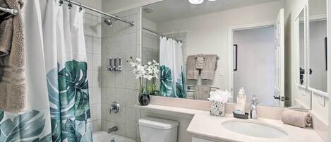 A modern bathroom with a shower curtain, toilet, sink, and a large mirror.