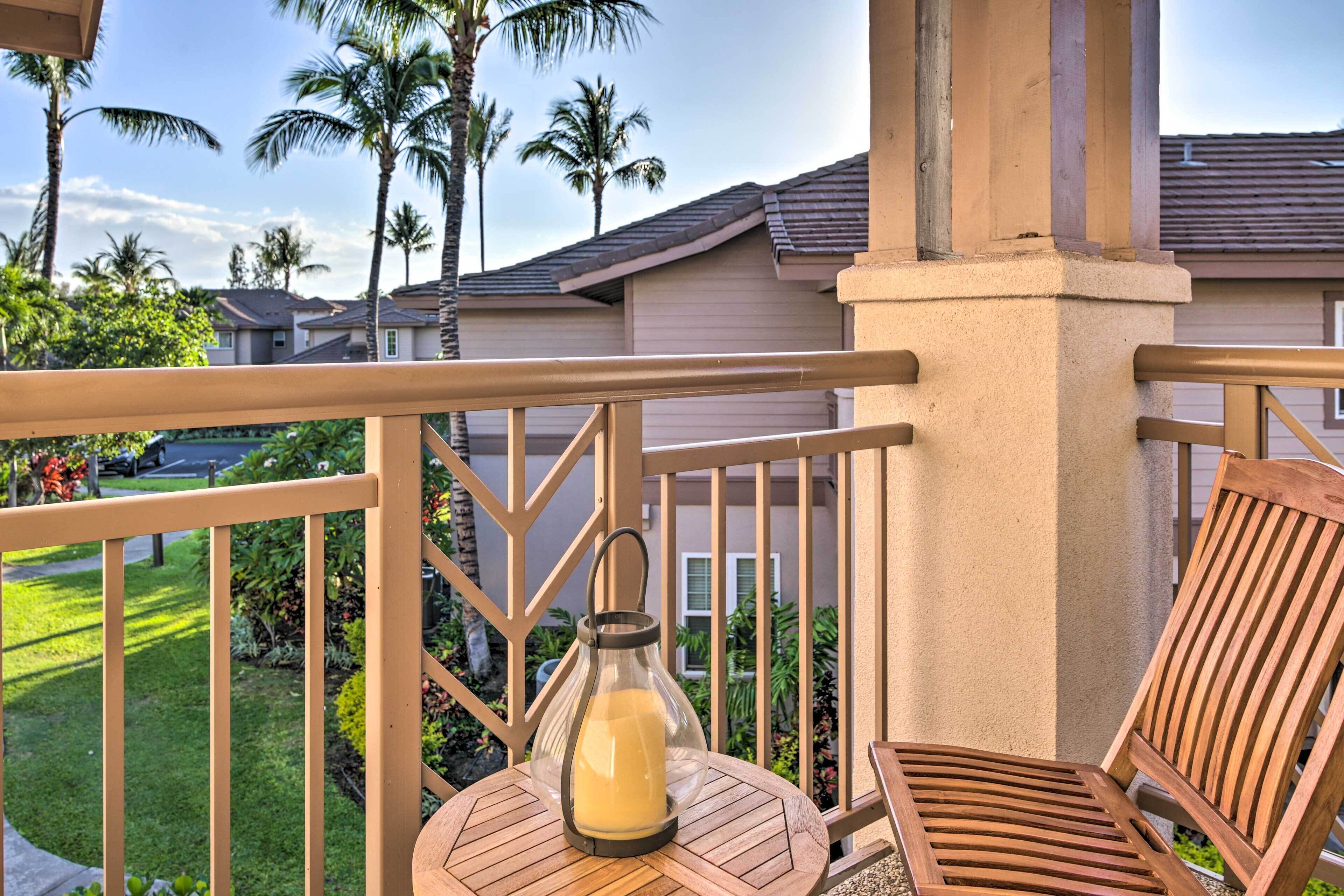 A wooden deck with a glass lantern table and a chair, overlooking a residential area with palm trees and houses.