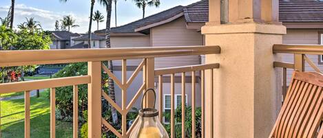A wooden deck with a glass lantern table and a chair, overlooking a residential area with palm trees and houses.