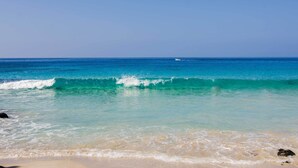 A beach with clear turquoise water, gentle waves, and a distant boat.