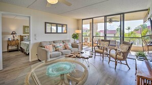 A spacious living room with a ceiling fan, a glass coffee table, a sofa, and wicker chairs.