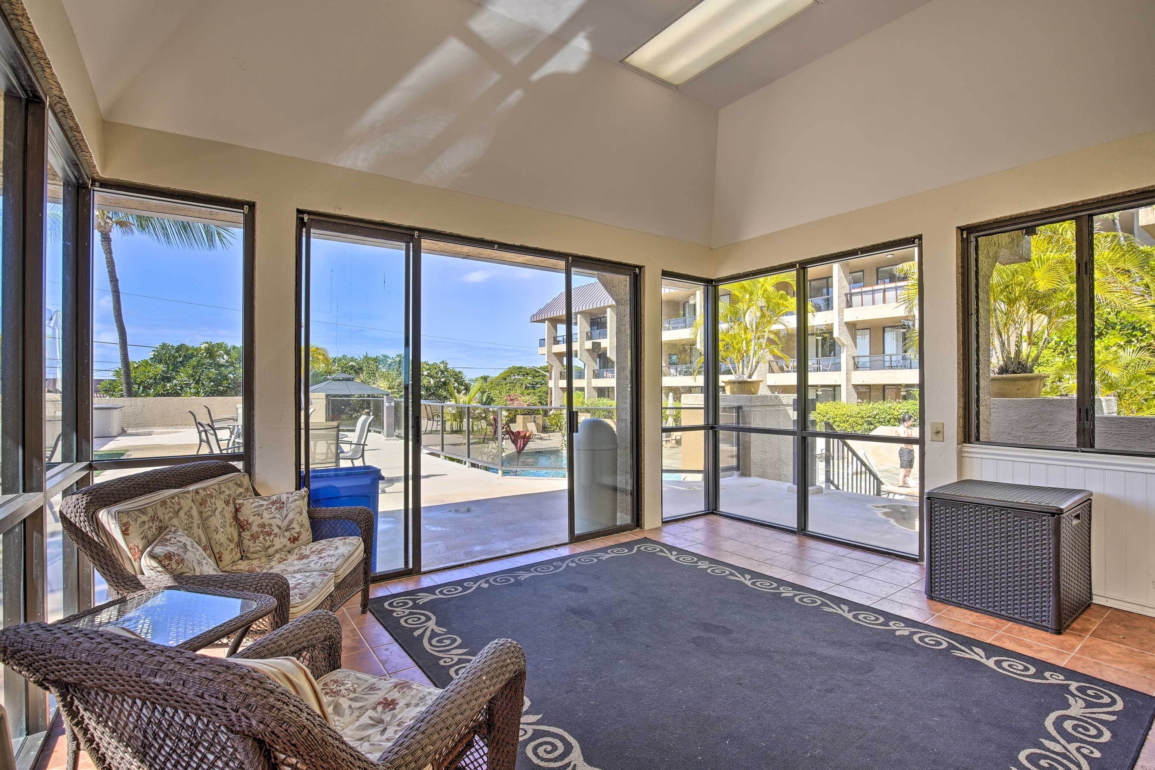 A spacious balcony with wicker furniture, a black rug, and a view of a pool and building.