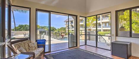 A spacious balcony with wicker furniture, a black rug, and a view of a pool and building.
