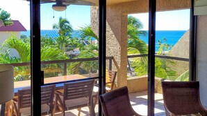 A balcony with a view of the ocean, wooden furniture, and tropical plants.
