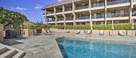A hotel with a swimming pool, outdoor seating, and a multi-story building with balconies.