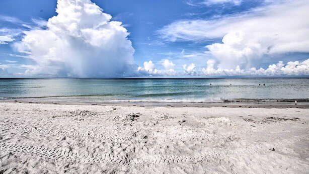 Ein Strand mit blauem Himmel und großen Wolken.